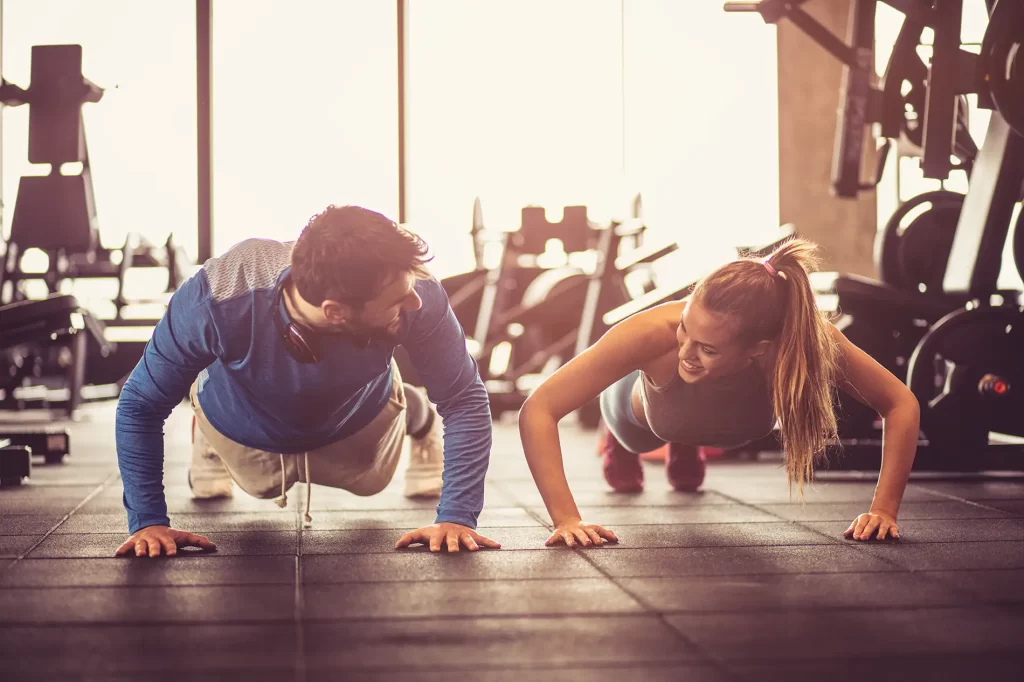 Man and a woman doing pushups in a gym.