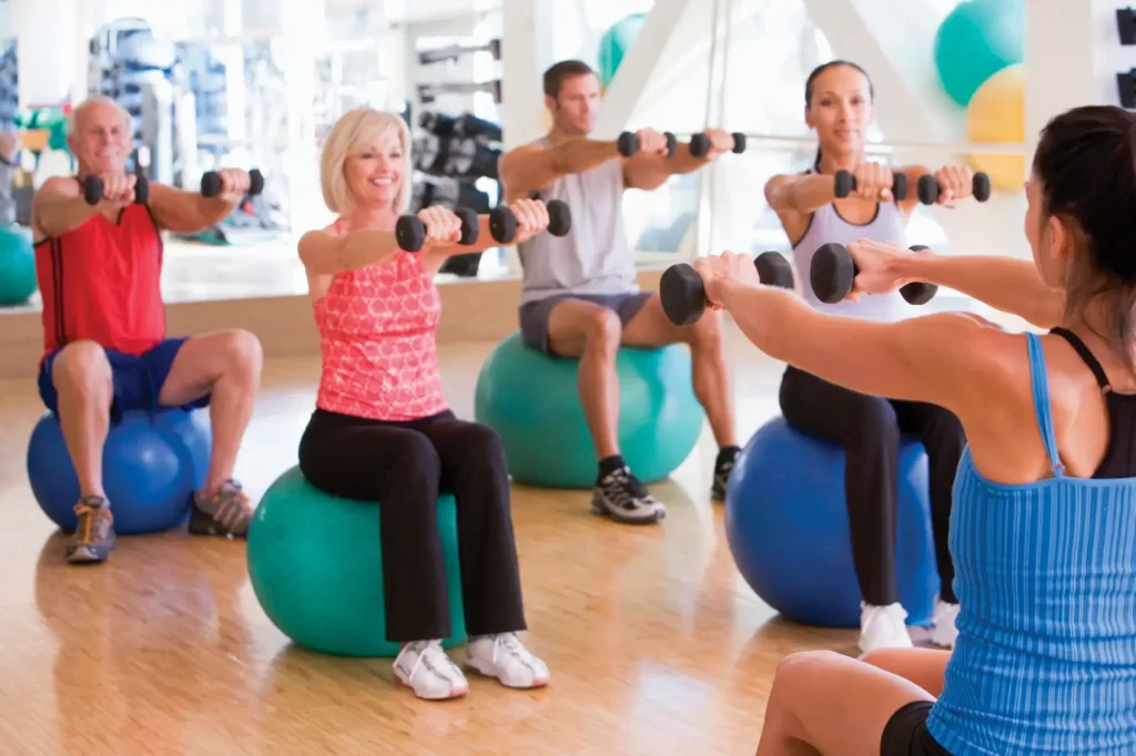 People in a workout class in yoga balls lifting weights.