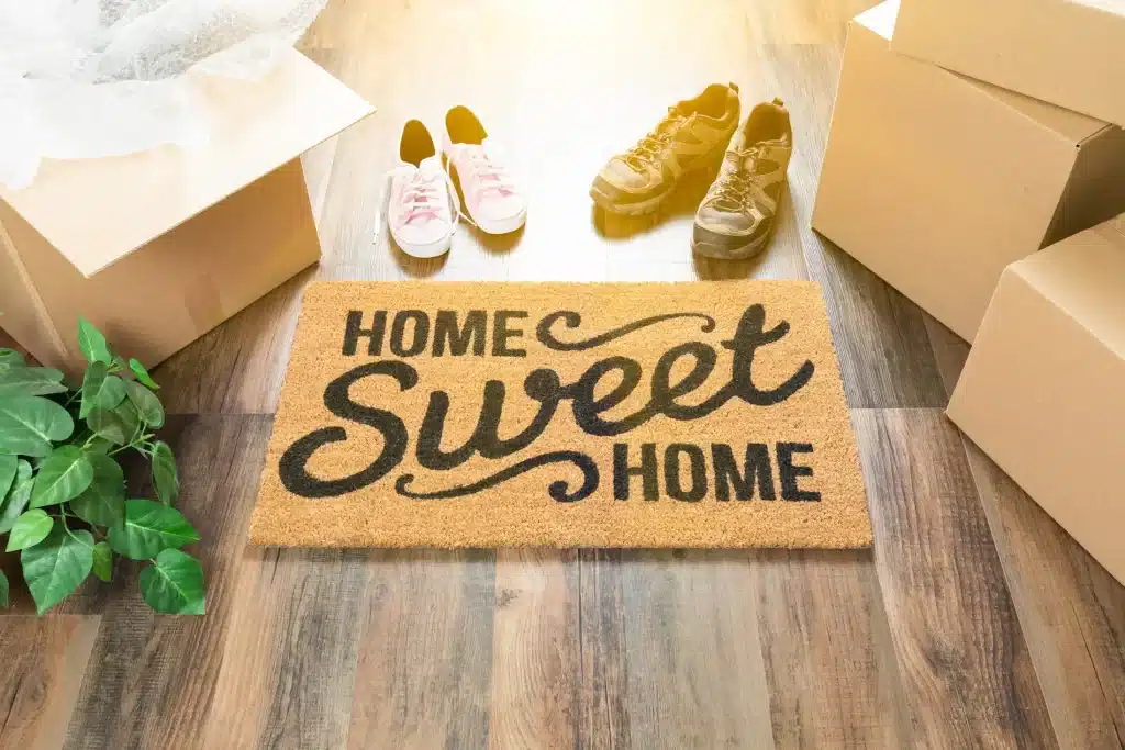 Moving boxes and welcome mat that says Home Sweet Home to show the concept of moving in to a new home.