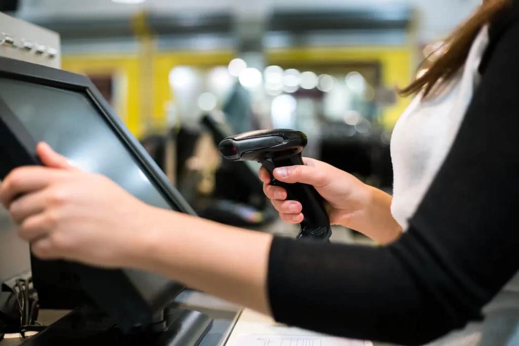 Retail store associate scanning items at checkout using a modern point of sale (POS) system for customer purchase processing.