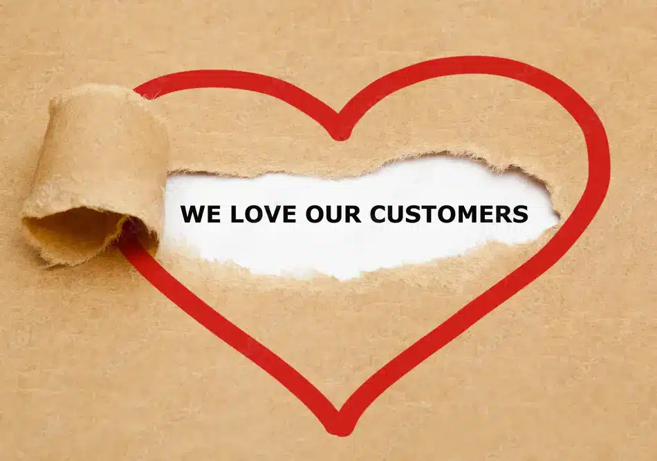 Customer appreciation concept depicted by the torn paper exposing the phrase "we love our customers" surrounded by a marker drawn red heart.