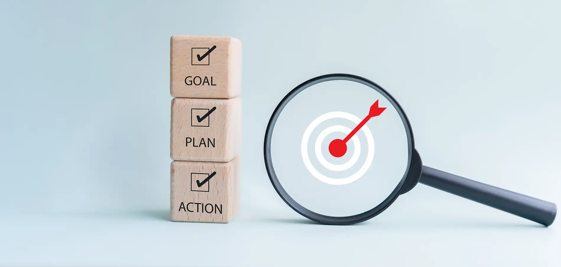 Goal, plan, and action concept showing wooden blocks with check marks and magnifying glass showing a target in the middle.
