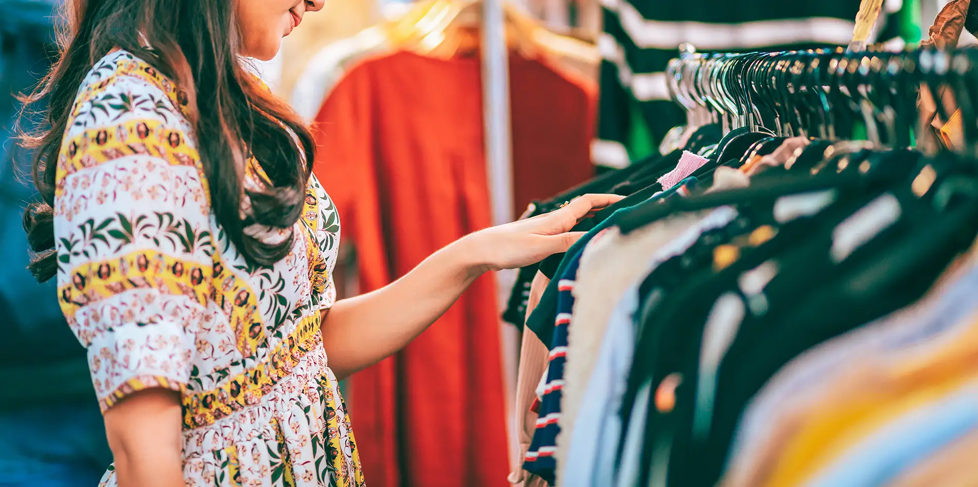 Female shopper browsing clothes on a round clothing rack in a fashion retail store.